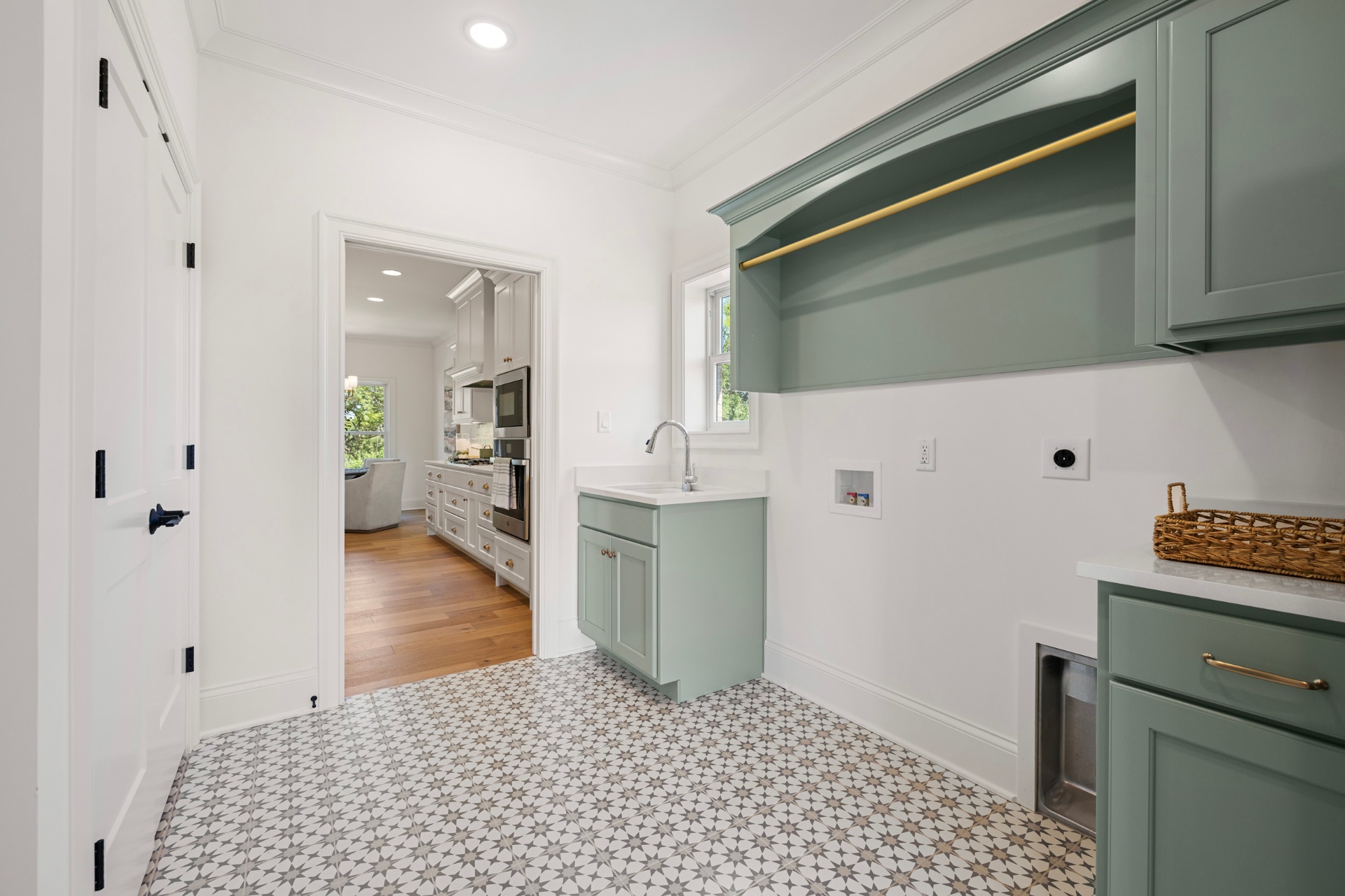 Laundry room with sage cabinetry and patterned tile